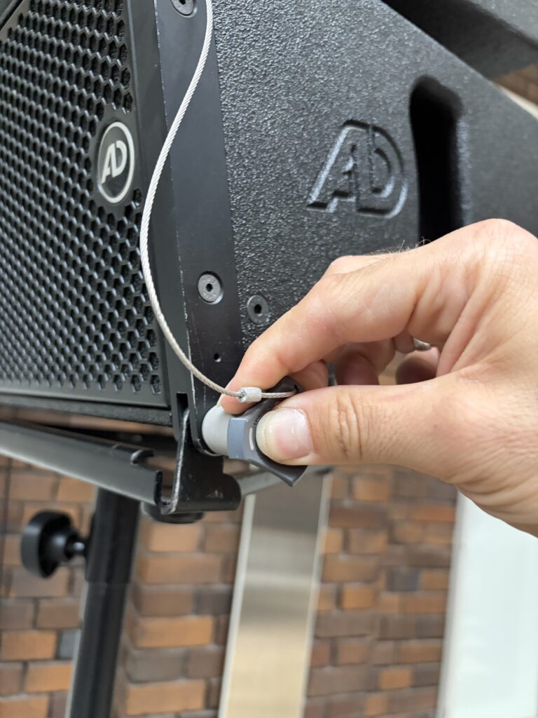 Nahaufnahme einer Hand beim Einstecken eines Steckverbinders an einem AD-PA-Lautsprecher mit sichtbarem Sicherungsseil.